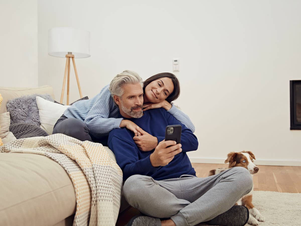 Ein Paar sitzt mit einer Decke vor einer Couch und bedient ein Handy