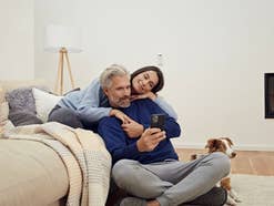 Ein Paar sitzt mit einer Decke vor einer Couch und bedient ein Handy