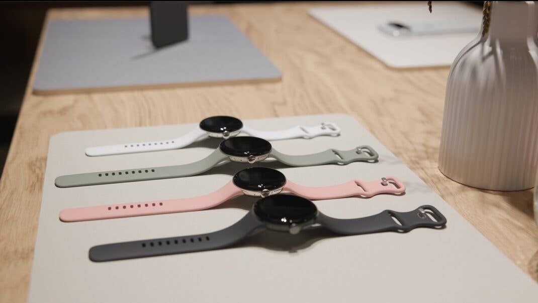 Vier Google Pixel Watches in verschiedenen Farben nebeneinander auf einem hellen Holztisch.