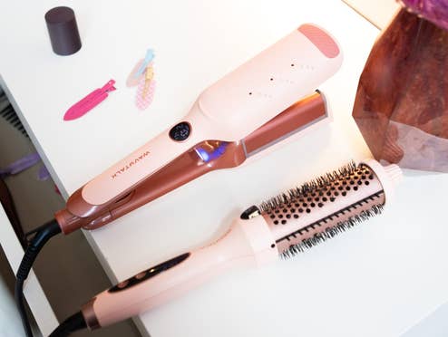 Zwei Produkte fürs Haarstyling der Firma Wavytalk liegen auf einem Tisch nebst Deko und Haarspangen