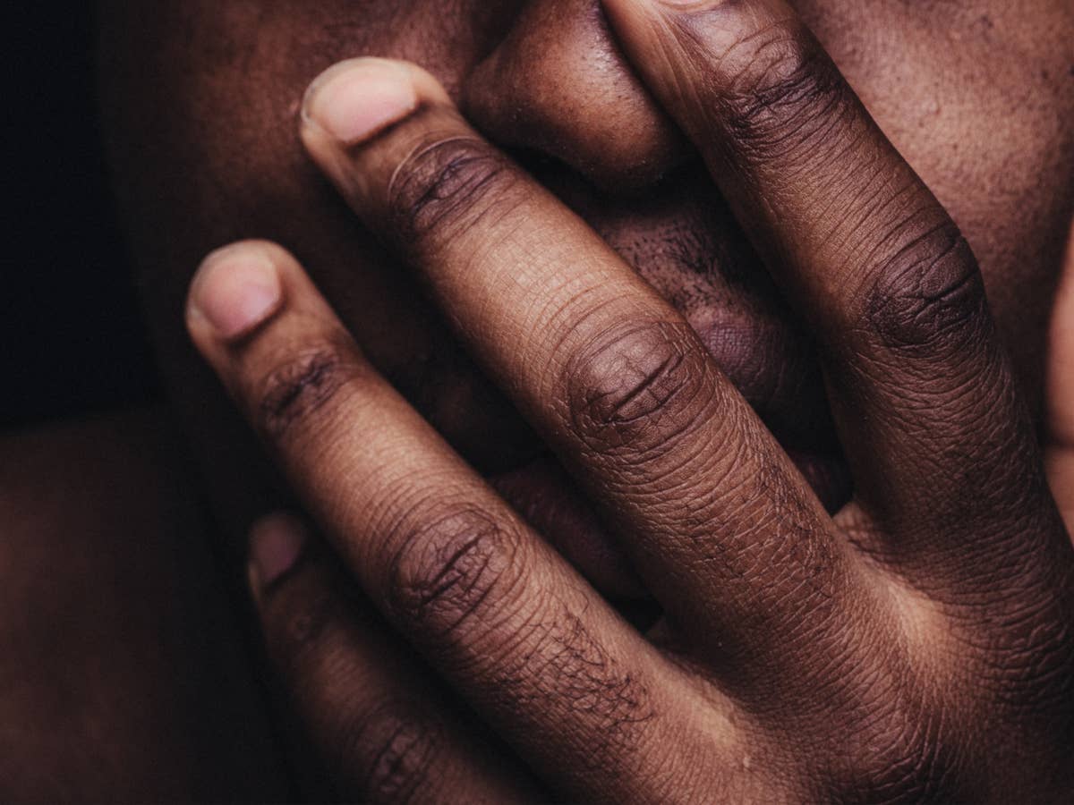 Eine schwarze Person hält sich die Hand vor dem Mund.