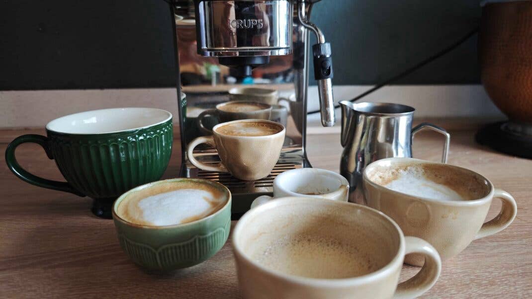 mehrere Tassen mit Kaffee und Milchschaum nebst Milchkännchen stehen vor der Krups Coffee Crush