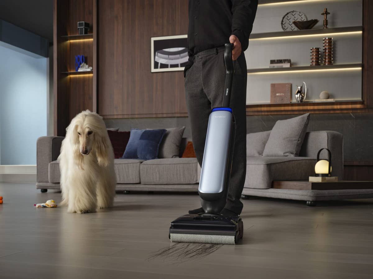 Ein Mann saugt seine Wohnung, neben ihm steht ein Hund