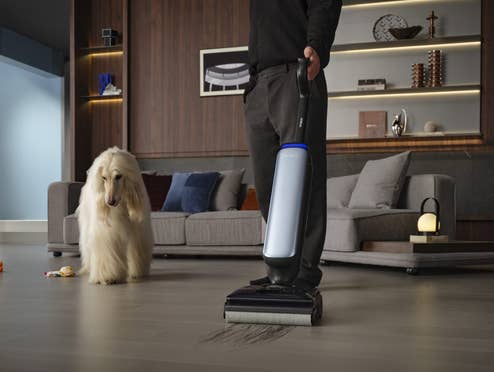 Ein Mann saugt seine Wohnung, neben ihm steht ein Hund