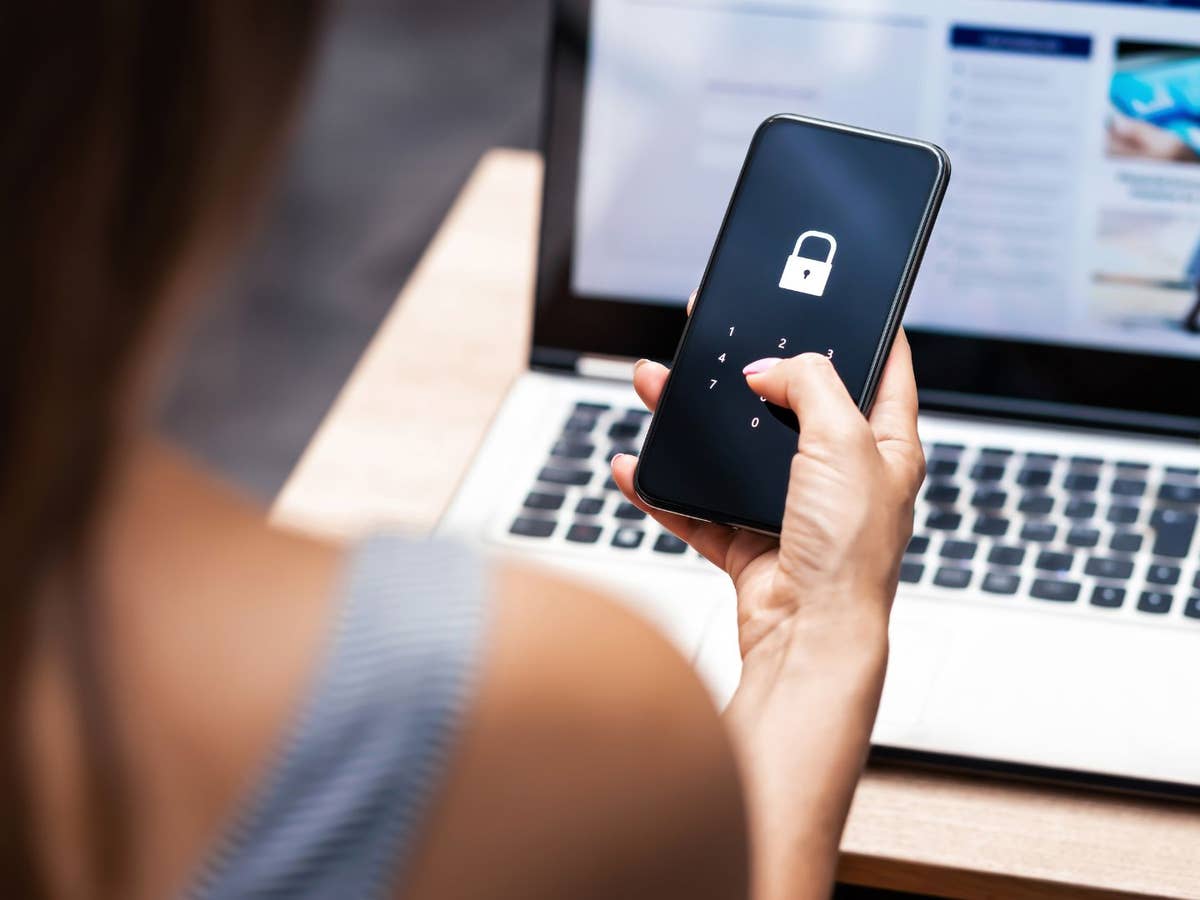 2-Faktor-Authentifizierung Eine Frau sitzt vor einem Laptop und hat ein Handy mit einer Authenticator-App in der Hand