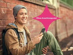 Mann sitzt vor einer Mauer mit einem Handy in der Hand