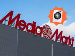 Ein MediaMarkt-Gebäude vor blauem Himmel. Davor sieht man eine Samsung-Waschmaschine.