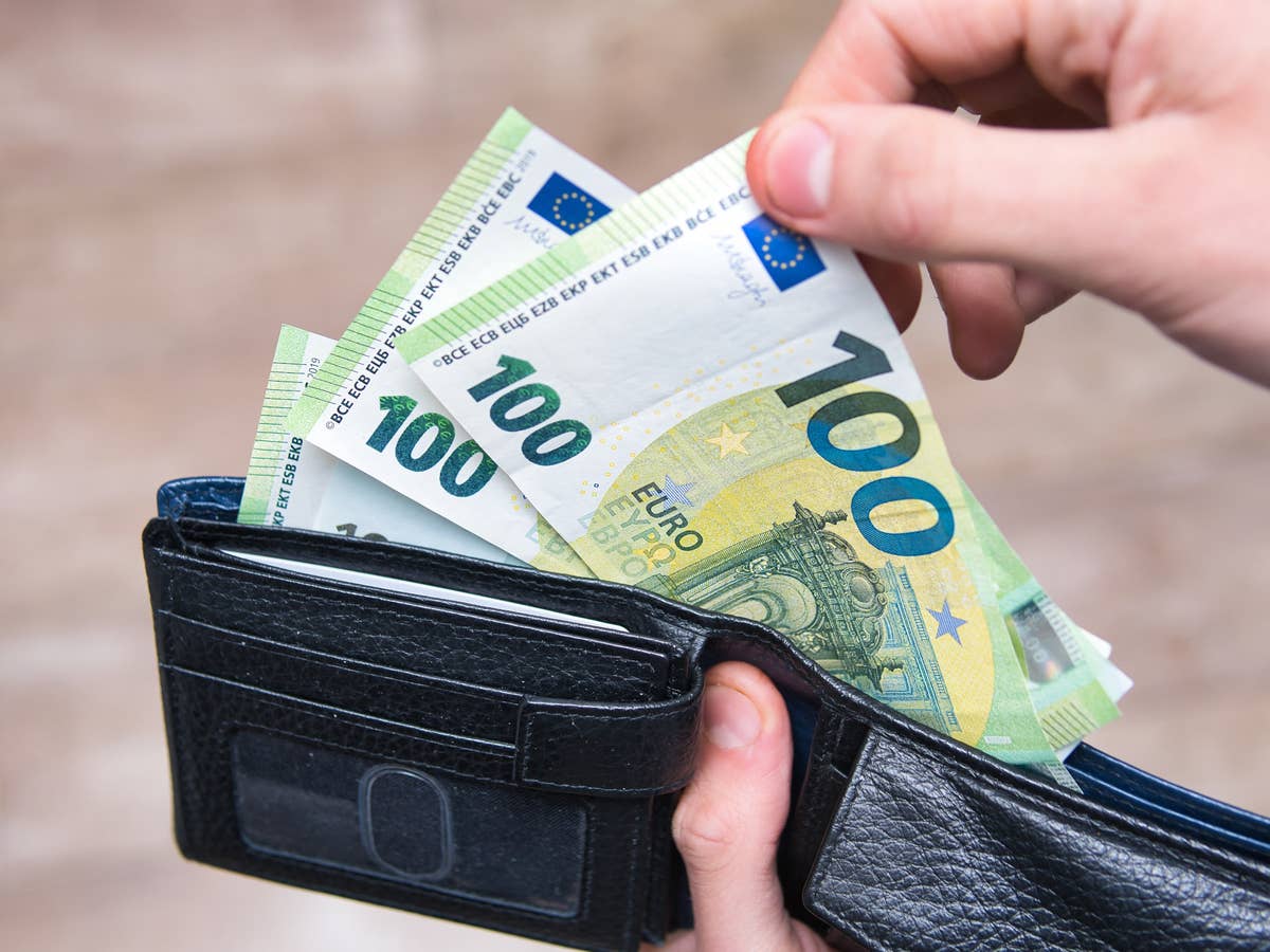 Hand zieht 100-Euro-Scheine aus einer Geldbörse.