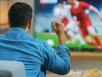 Mann sieht Fußballspiel auf einem Fernseher und jubelt dabei.