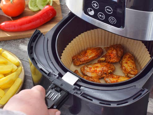 Spezielle Lebensmittel für den Airfryer sind gerade total in, aber brauchst du sie wirklich? Eine Person macht sich Essen im Airfryer und hat rund herum weitere Lebensmittel auf dem Küchentisch stehen.