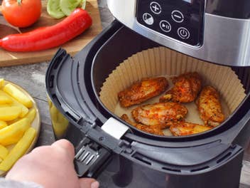 Eine Person macht sich Essen im Airfryer und hat rund herum weitere Lebensmittel auf dem Küchentisch stehen.
