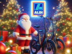 Weihnachtsmann steht neben Fahrrädern und vor Weihnachtsbäumen sowie einen Aldi-Logo an der Wand.