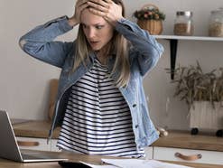 Eine Frau steht vor ihrem Laptop und ist schockiert