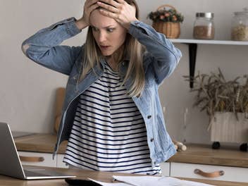 Eine Frau steht vor ihrem Laptop und ist schockiert
