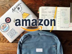 Amazon-Logo vor einem Laptop, einer Schultasche und einem Notizblock