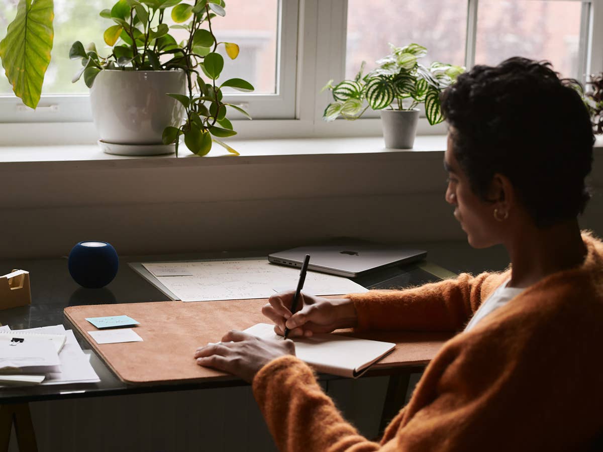Apple HomePod mini und Mac auf einem Schreibtisch neben einer Person