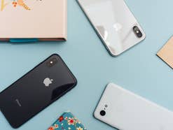 Smartphones von Apple und anderen Herstellern liefen auf einer blauen Unterlage zusammen mit einem Notizbuch und mehreren bunten Blättern aus Papier