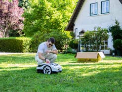 Person schaltet den Raccoon 2 SE Mähroboter per Knopfdruck im Garten an