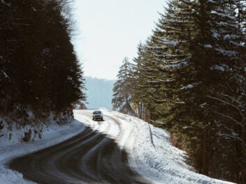 Ein Auto fährt auf einer Straße, die von Tannen gesäumt ist und die von Schnee bedeckt ist.