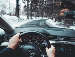 Ein Mensch fährt mit dem Auto, die Hände auf dem Lenkrad, draußen eine winterliche Landschaft.
