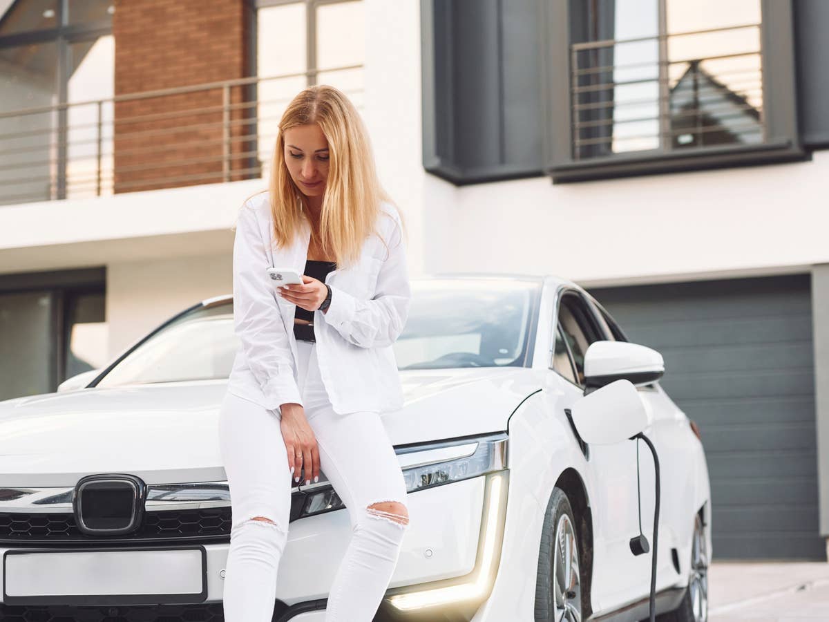 Frau sitzt auf der Motorhaube eines E-Autos.