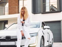 Frau sitzt auf der Motorhaube eines E-Autos.