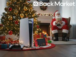 Verschiedene Konsolen stehen vor einem Weihnachtsbaum. Im Hintergrund zählt ein Weihnachtsmann Geld und ein Back Market-Logo ist in der rechten oberen Ecke zu erkennen.