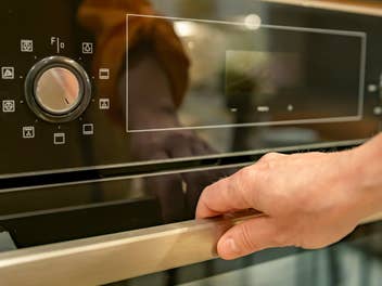 eine Hand will einen Backofen öffnen, man sieht die Symbole auf dem Gerät und den Drehregler