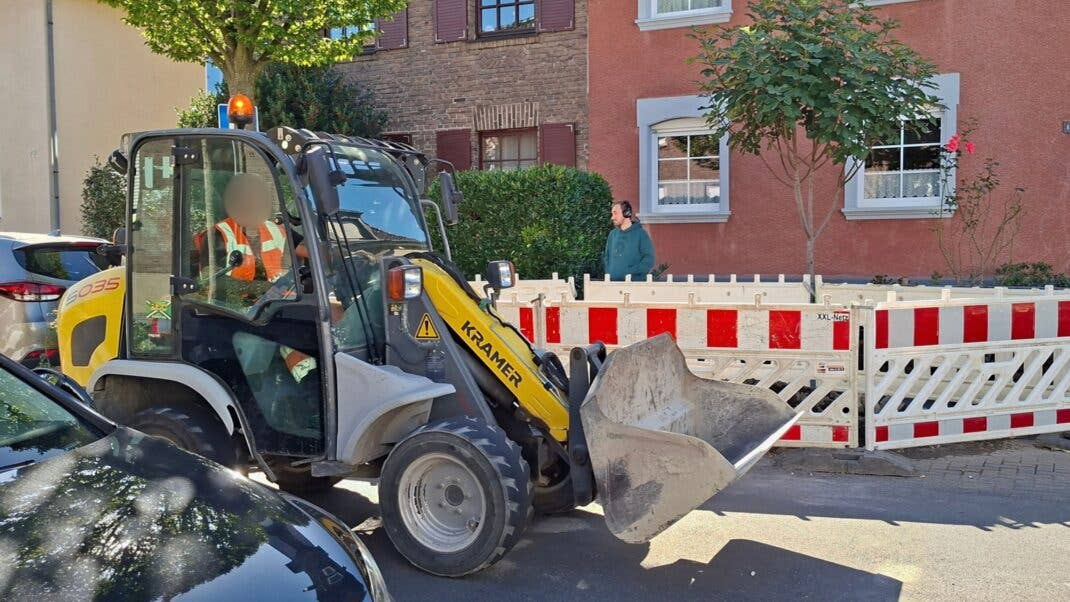 Bagger fährt vor einer Baustelle, im Hintergrund Redakteur Cedric Litzki mit EarFun Wave Pro X