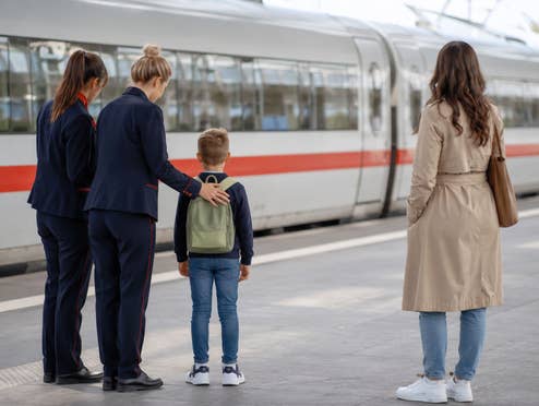 Ein Kind steht am Bahnsteig mit 2 Bahn-Mitarbeitern und seiner Mutter