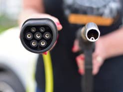 Ladeanschluss und Zapfhahn nebeneinander - gehalten von einer Frau.