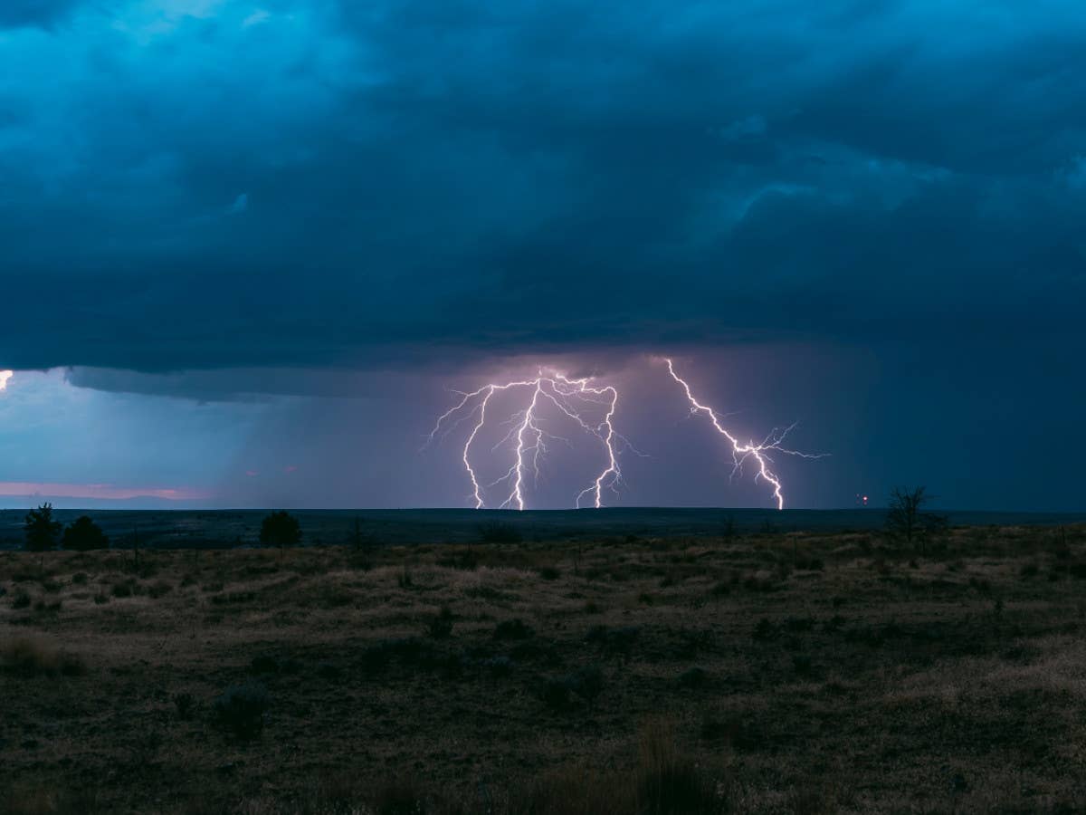 Aus dunklen Gewitterwolken schlägt ein Blitz in den Boden ein