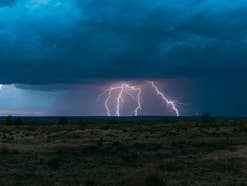 Aus dunklen Gewitterwolken schlägt ein Blitz in den Boden ein