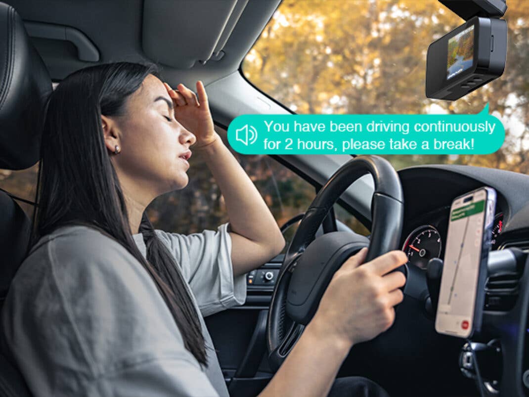 Eine erschöpfte Person fährt Auto und eine Dashcam gibt eine Warnung wegen zu langer Fahrtzeit aus.