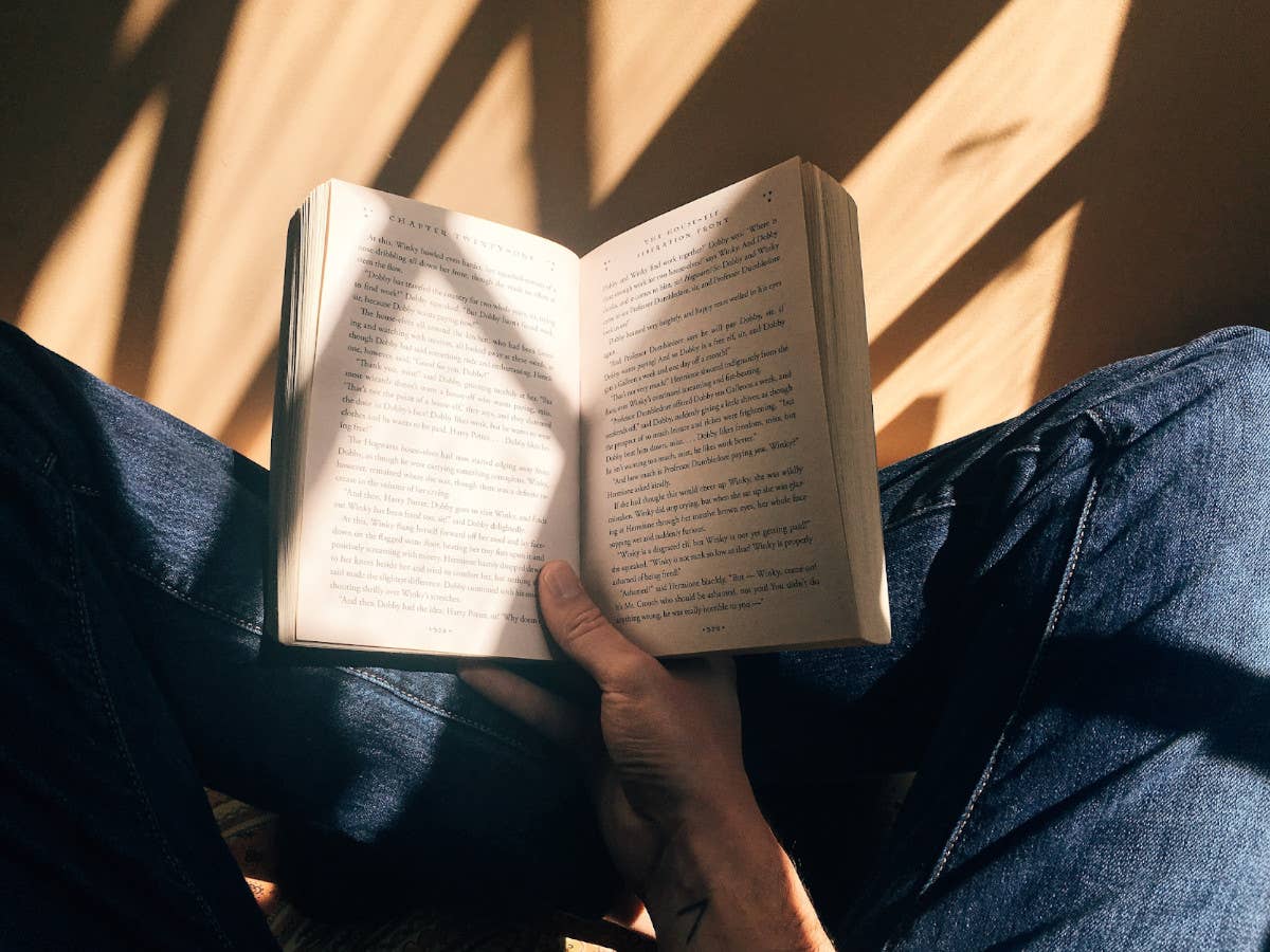 Eine Person sitzt auf einem Holzboden und hält ein geöffnetes Buch in der Hand.