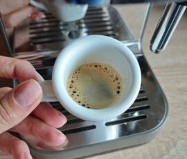 Der Espresso hat nicht viel Crema, aber mit der richtigen Bohne wird es besser. Hand hält Espresso in Tasse vor Krups Coffee Crush Maschine