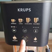So sieht das Display der Coffee Crush Experience von Krups aus. Display der Krups Coffee Crush eingeschaltet mit Symbolen und Finger zeigt auf Start/Stopp