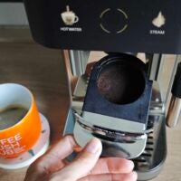 Nach dem Durchlauf muss der Kaffeesatz entsorgt werden. Hand holt Behälter mit Kaffee-Puck aus der Krups Coffee Crush