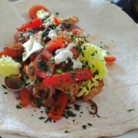 Das Ergebnis garniert mit Salat und Soße im Wrap. Wrap auf Teller mit Fleisch, paprika, Salat, Zwiebeln und Soße garniert
