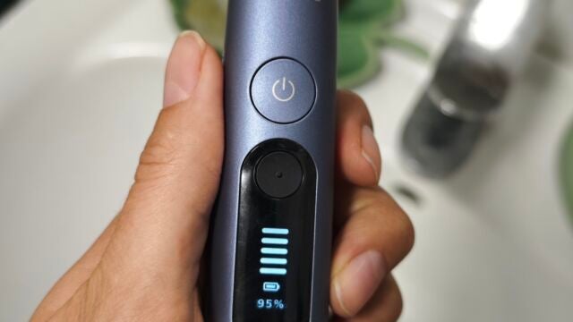 Batterieanzeige Hand hält Philips Sonicare Next-Generation DiamondClean 9900 Prestige über dem Waschbecken