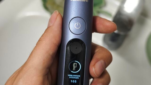 Bürstenkopfwechsel-Erinnerung Hand hält Philips Sonicare Next-Generation DiamondClean 9900 Prestige über dem Waschbecken