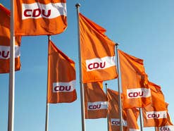 Orangene CDU-Fahnen vor blauem Himmel im Wind.