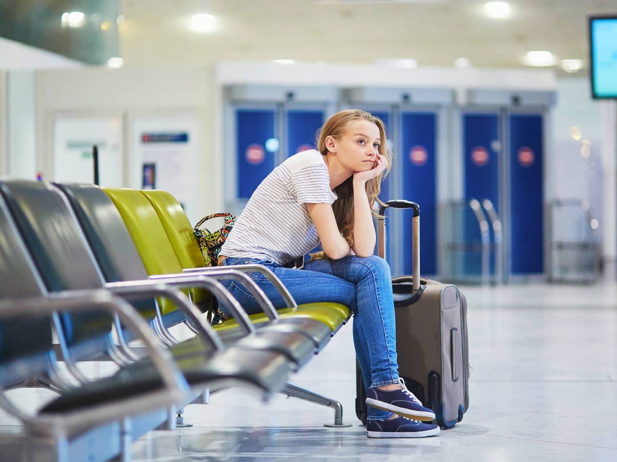 Frau sitzt an einem Flughafen mit Gepäck und schaut traurig.