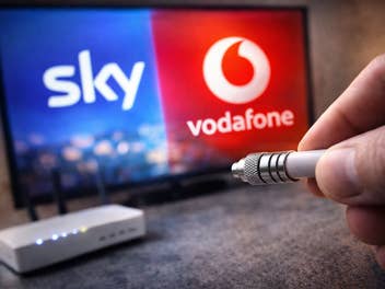 Die Logos von Sky und Vodafone auf einem TV, im Vordergrund ein Kabel