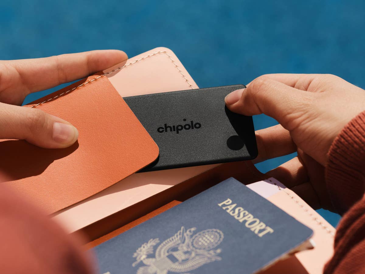 Eine Person hält einen Chipolo-Karten-Tracker in der Hand, neben einem Reisepass und Geldbörse.