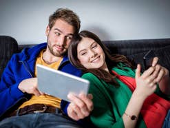 Paar surft auf dem Sofa mit Tablet und Smartphone im Internet