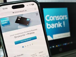 Mobile Website der Consorsbank vor einem Logo der Bank auf einem Notebook-Bildschirm.