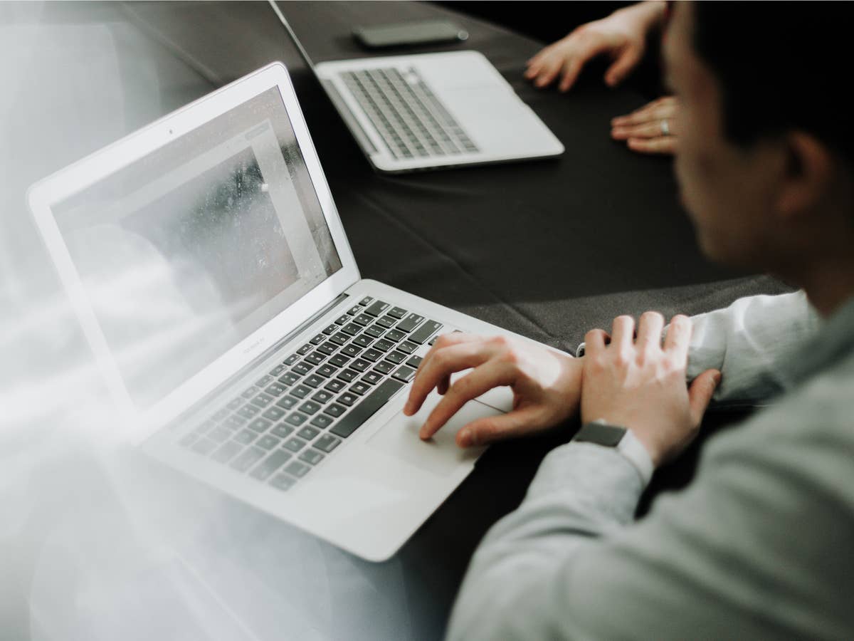 Person sitzt an Tisch und arbeitet an einem Laptop