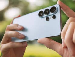 Zwei Hände halten das Galaxy S26. Im Hintergrund ist eine Grünfläche zu sehen.