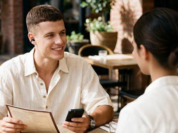 Ein Mann mit einem Kopfhörer im Ohr unterhält sich mit einer Person in einem Restaurant